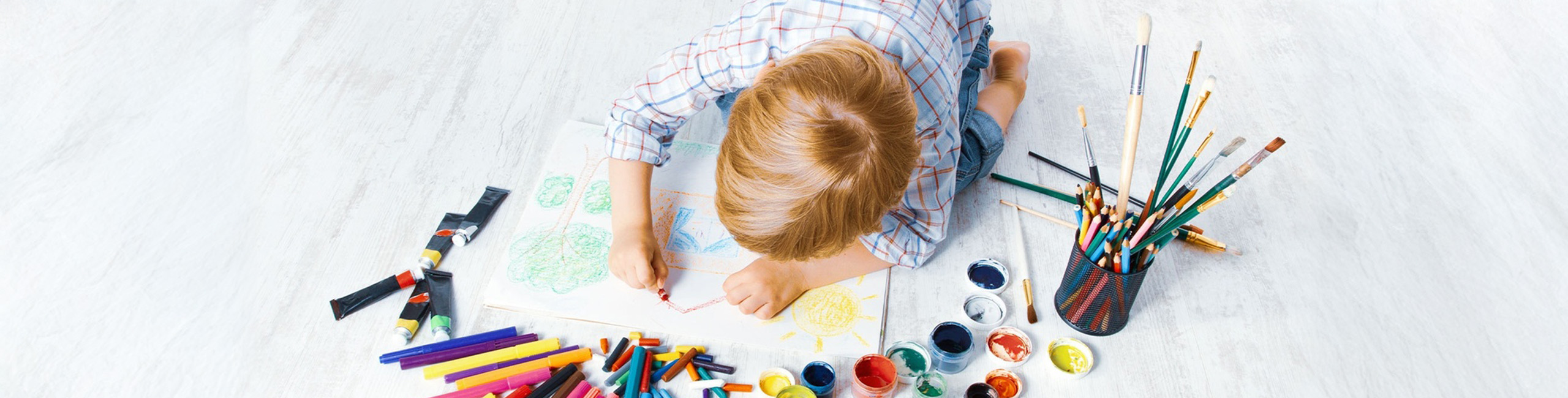 Дете си играе с пастели на пода.
