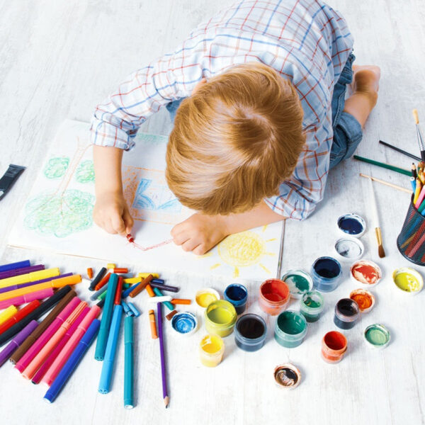 Дете си играе с пастели на пода.