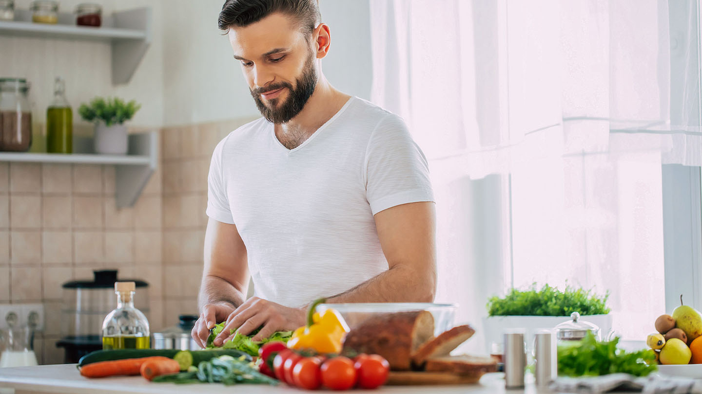 Мъж спортист приготвя здравословна храна в кухнята.
